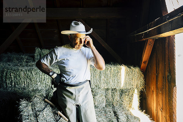 Kaukasischer Bauer in einer Scheune  der mit einem Handy telefoniert