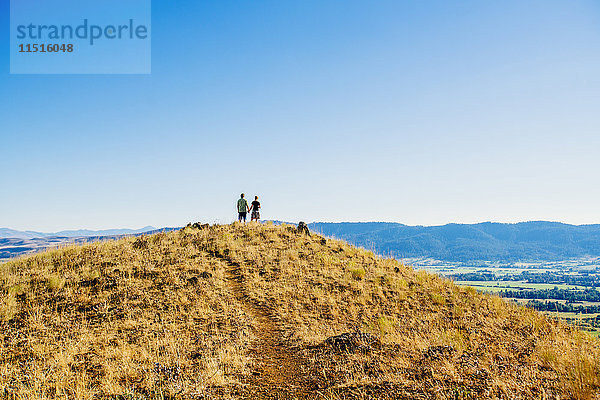 Entferntes kaukasisches Paar steht auf einem Hügel und hält sich die Hände
