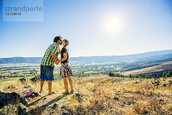 Kaukasisches Paar steht auf einem Hügel und küsst sich