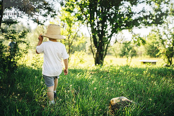 Kaukasischer Junge mit Hut  der im Gras läuft