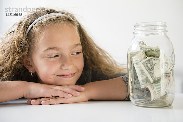 Lächelndes Mädchen spart Geld in einem Gefäß