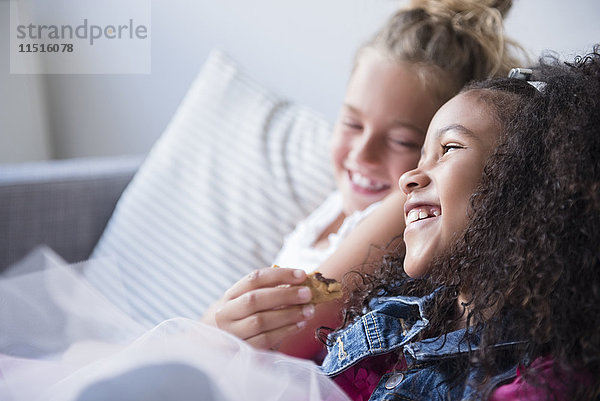 Lächelnde Mädchen essen Kekse auf dem Sofa