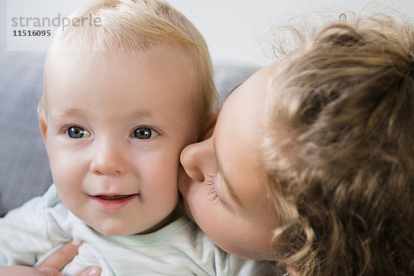 Lächelndes kaukasisches Mädchen küsst kleinen Bruder auf die Wange