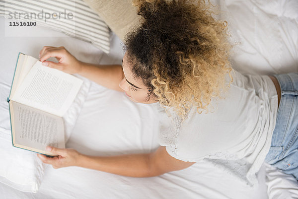 Gemischtrassige Frau liegt auf dem Bett und liest ein Buch
