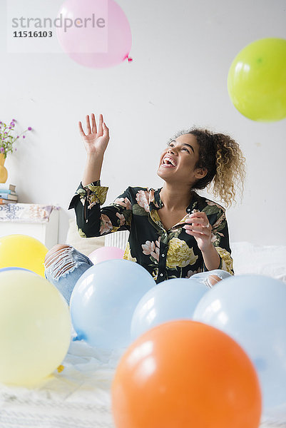Mixed Race Frau sitzt auf dem Bett und spielt mit Luftballons