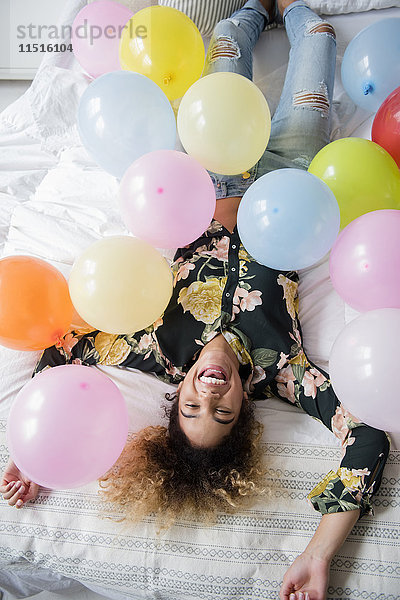 Gemischtrassige Frau auf dem Bett liegend  bedeckt mit Luftballons