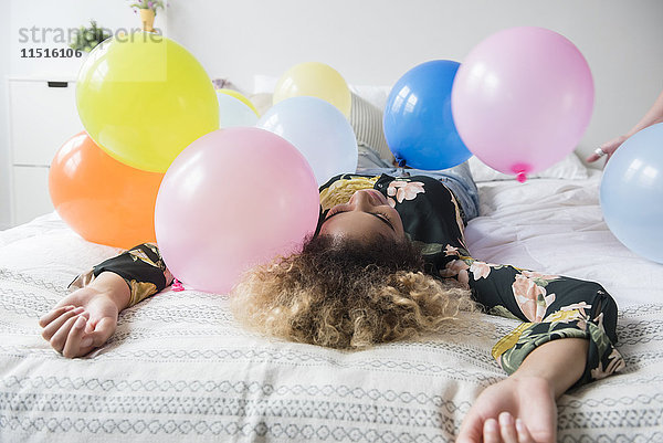 Gemischtrassige Frau sitzt auf einem mit Luftballons bedeckten Bett