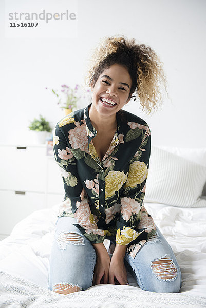 Lächelnde Mixed Race Frau kniend auf dem Bett