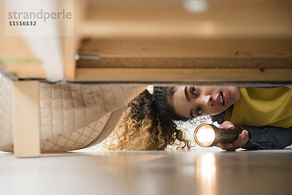 Gemischtrassige Frau sucht mit Taschenlampe unter dem Bett
