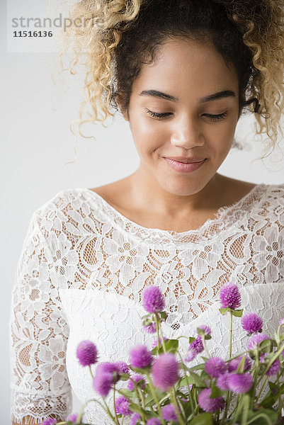 Gemischtrassige Frau im Hochzeitskleid bewundert den Blumenstrauß