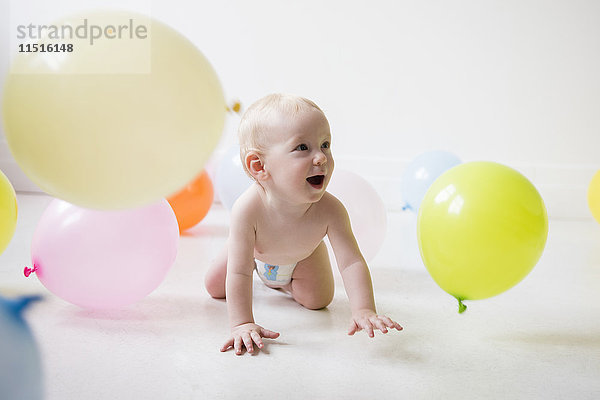 Kaukasisches Baby Junge krabbeln auf dem Boden beobachten Ballons