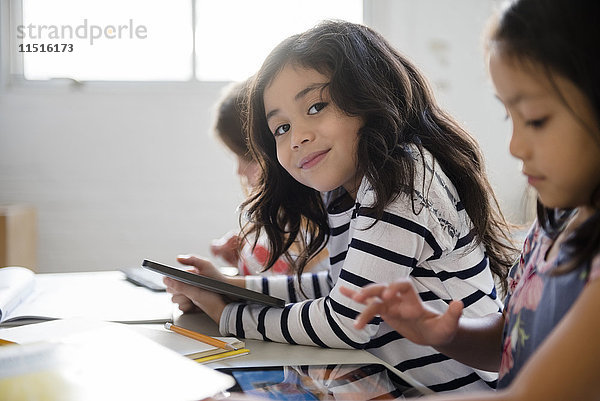 Porträt eines lächelnden Mädchens  das ein digitales Tablet im Klassenzimmer benutzt