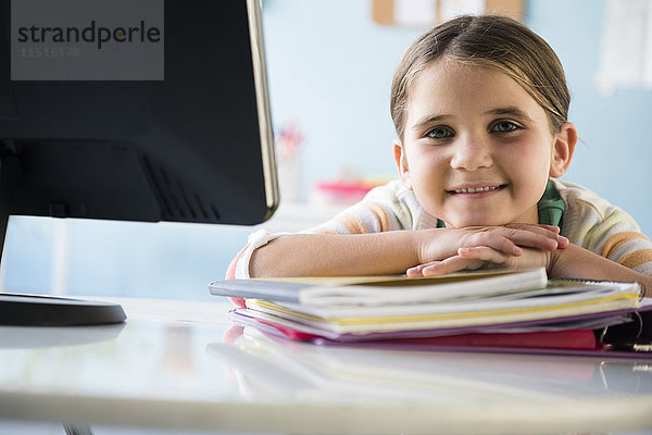 Lächelndes kaukasisches Mädchen  das sich auf Notebooks am Schreibtisch stützt