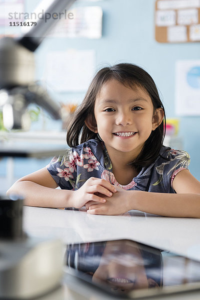 Lächelndes asiatisches Mädchen  das am Schreibtisch posiert