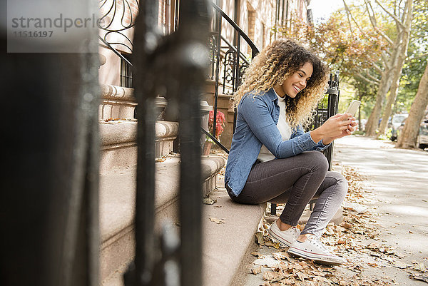 Gemischtrassige Frau in der Stadt  die eine SMS auf ihrem Mobiltelefon schreibt