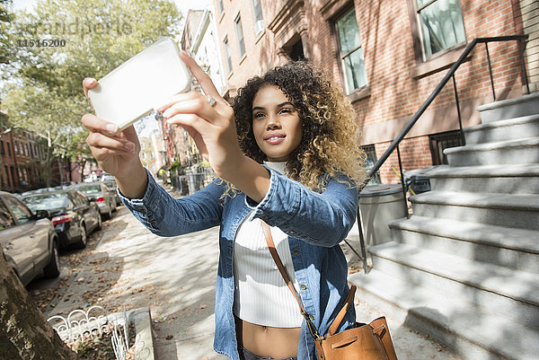 Gemischtrassige Frau in der Stadt  die für ein Selfie mit ihrem Handy posiert