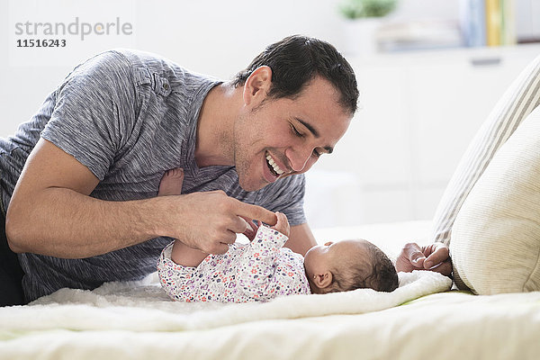 Hispanischer Vater liegt auf dem Bett und spielt mit seiner kleinen Tochter
