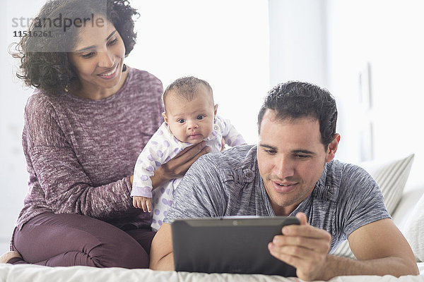 Hispanische Mutter und Vater mit kleiner Tochter  die auf ein digitales Tablet schauen