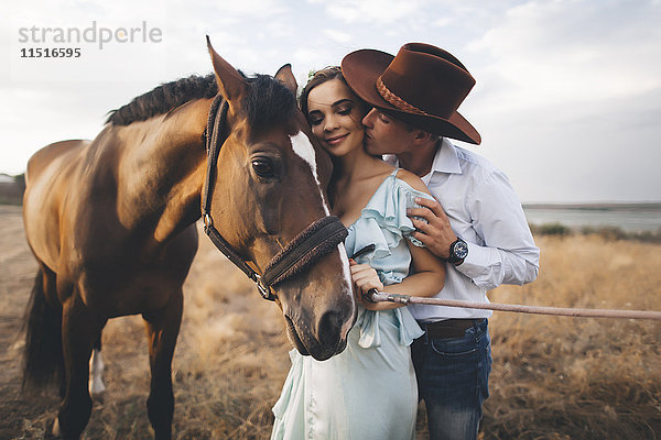 Kaukasischer Cowboy küsst Frau auf die Wange in der Nähe des Pferdes