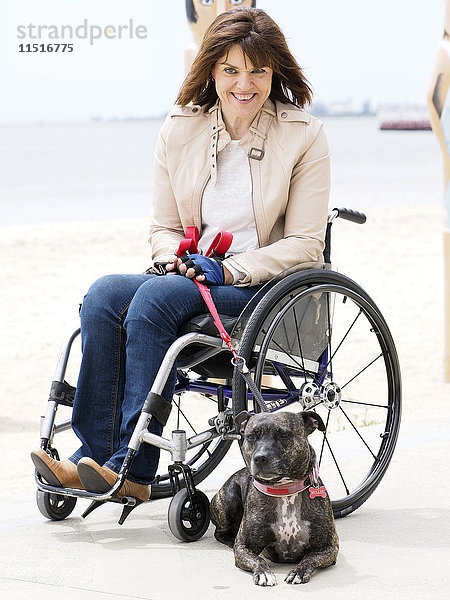 Frau im Rollstuhl sitzend am Wasser mit Hund an der Leine