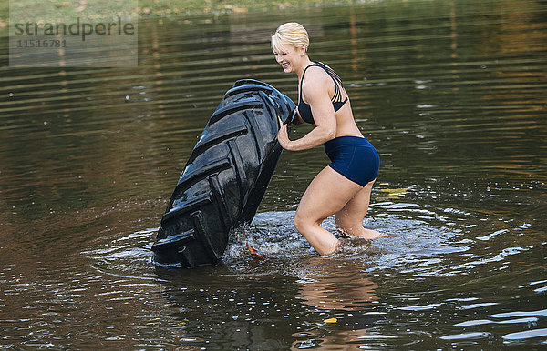 Kaukasische Frau  die einen schweren Reifen in einen See schiebt
