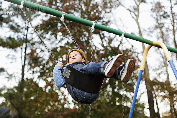 Gemischtrassiger Junge auf Spielplatzschaukel