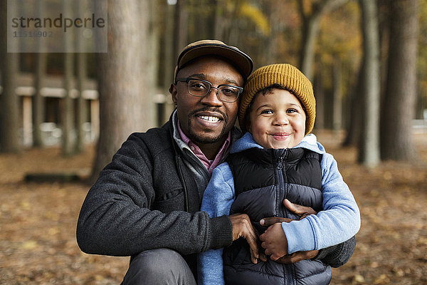 Porträt von lächelndem Vater und Sohn  die sich im Park umarmen
