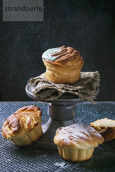 Selbstgemachte Cruffins (eine Kreuzung aus Croissant und Muffin) mit Zuckerguss auf einem grauen Kuchenständer