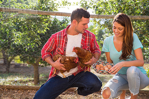 Paar aus biologischer Landwirtschaft  das Freilandhühner und einen Korb mit Eiern hält
