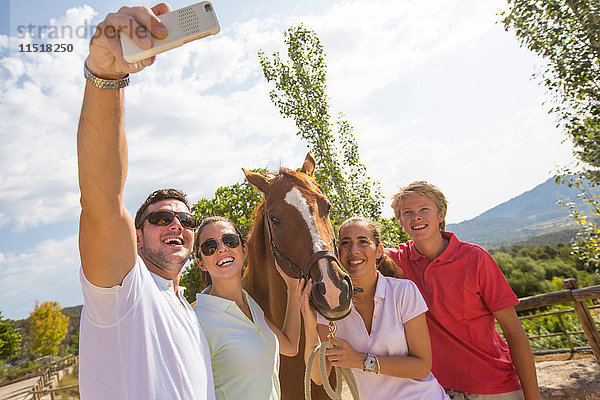 Stallbursche und Freunde nehmen Smartphone-Selfie mit Pferd in ländlichen Ställen