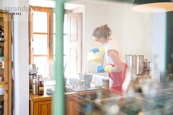 Junge Frau gießt flüssige Lavendelseife in eine Schüssel in einer Werkstatt für handgemachte Seife