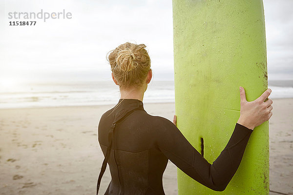 Weibliche Surferin hält ein Surfbrett in der Hand und blickt vom Rockaway Beach  New York  USA