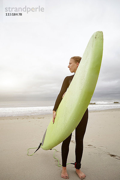 Surferin  die ein Surfbrett trägt  im Rückblick von Rockaway Beach  New York  USA