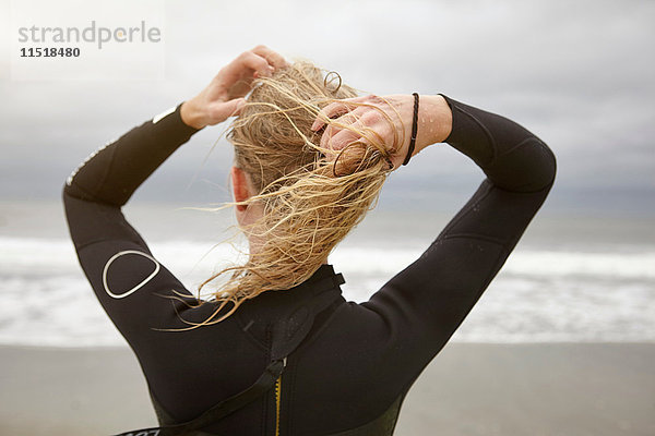 Rückansicht einer Surferin beim Binden nasser blonder Haare am Rockaway Beach  New York  USA