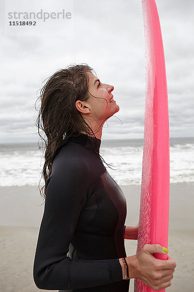 Porträt einer jungen Surferin mit rosa Surfbrett in der Hand am Rockaway Beach  New York  USA