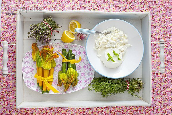 Ein Arrangement aus Zucchiniblüten  frischen Kräutern und Ricotta auf einem Tablett