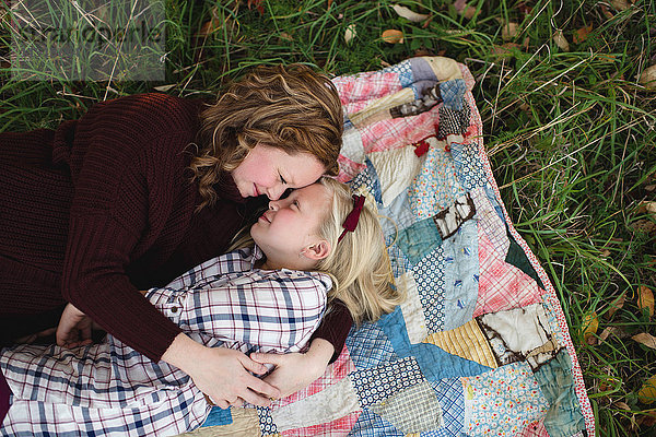 Mutter und Tochter liegen auf einer Decke und umarmen sich von Angesicht zu Angesicht