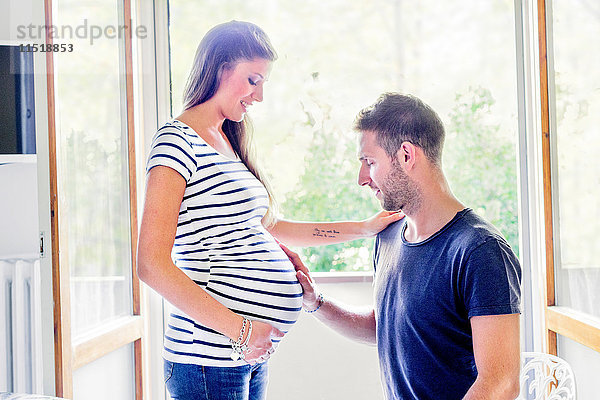 Mann berührt lächelnd den Bauch einer schwangeren Frau