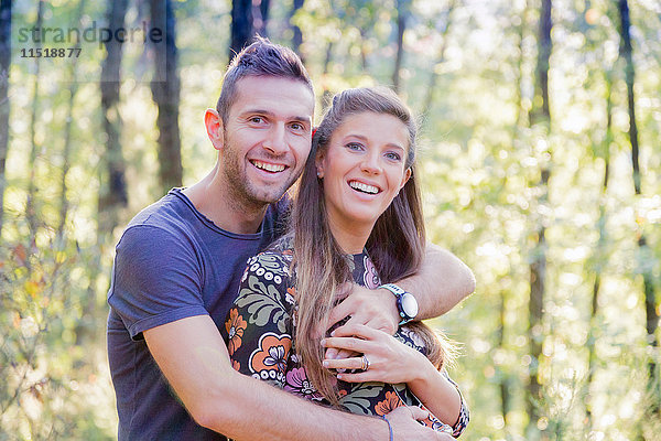 Paar im Wald umarmt sich und schaut lächelnd in die Kamera