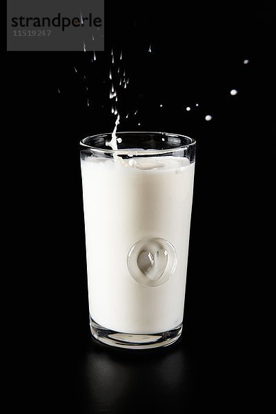 Ein Glas Milch mit einem Spritzer auf schwarzem Hintergrund