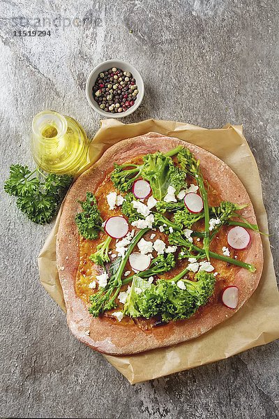 Pizza aus Rote-Bete-Teig mit Brokkoli  Salat  Radieschen und Feta  daneben Olivenöl  Pfeffer und Petersilie
