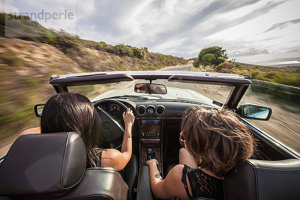 Zwei junge Frauen in einem Cabriolet  Fahrt auf einer Panoramastraße  Rückansicht