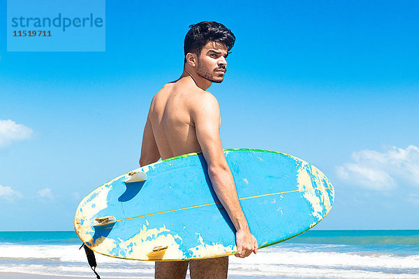 Junger Mann steht am Strand und hält ein Surfbrett  Fortaleza  Ceara  Brasilien
