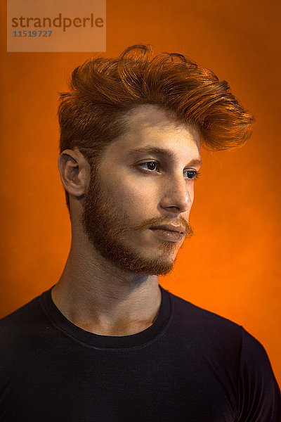 Porträt eines jungen Mannes mit roten Haaren vor orangem Hintergrund