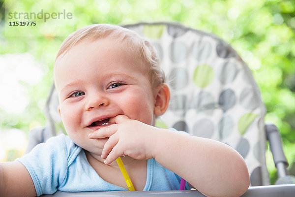 Porträt eines kleinen Jungen mit Fingern im Mund auf einem Hochstuhl im Garten