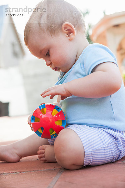 Kleiner Junge sitzt auf der Terrasse und spielt mit Spielzeug