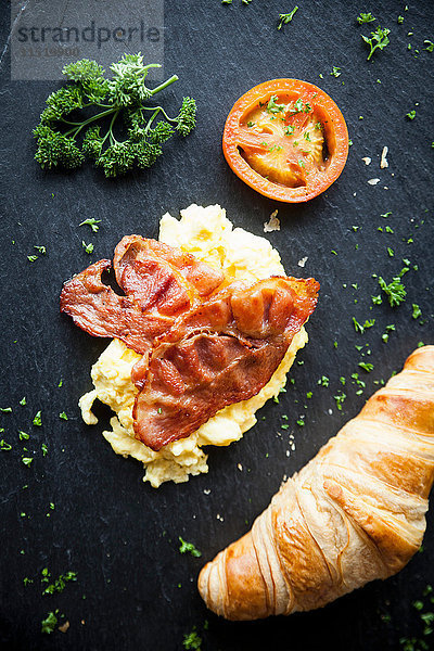 Draufsicht auf Croissant mit Speck  Omelett und Tomaten Frühstück auf Schiefer