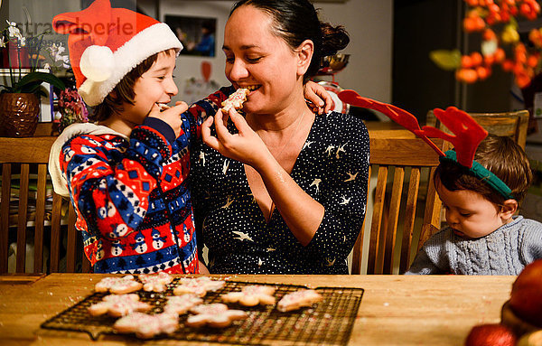 Mutter und zwei Söhne essen am Tisch selbstgebackene Weihnachtsplätzchen