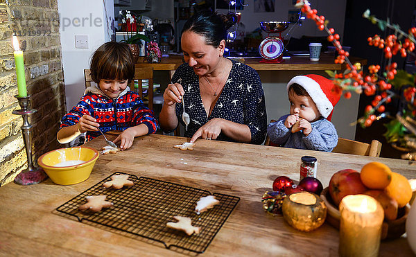 Mutter und zwei Söhne glasieren selbstgebackene Weihnachtsplätzchen am Tisch