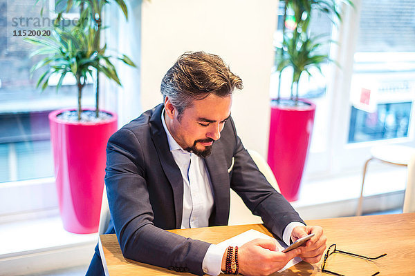 Geschäftsmann am Büroschreibtisch beim Lesen von Smartphone-Texten